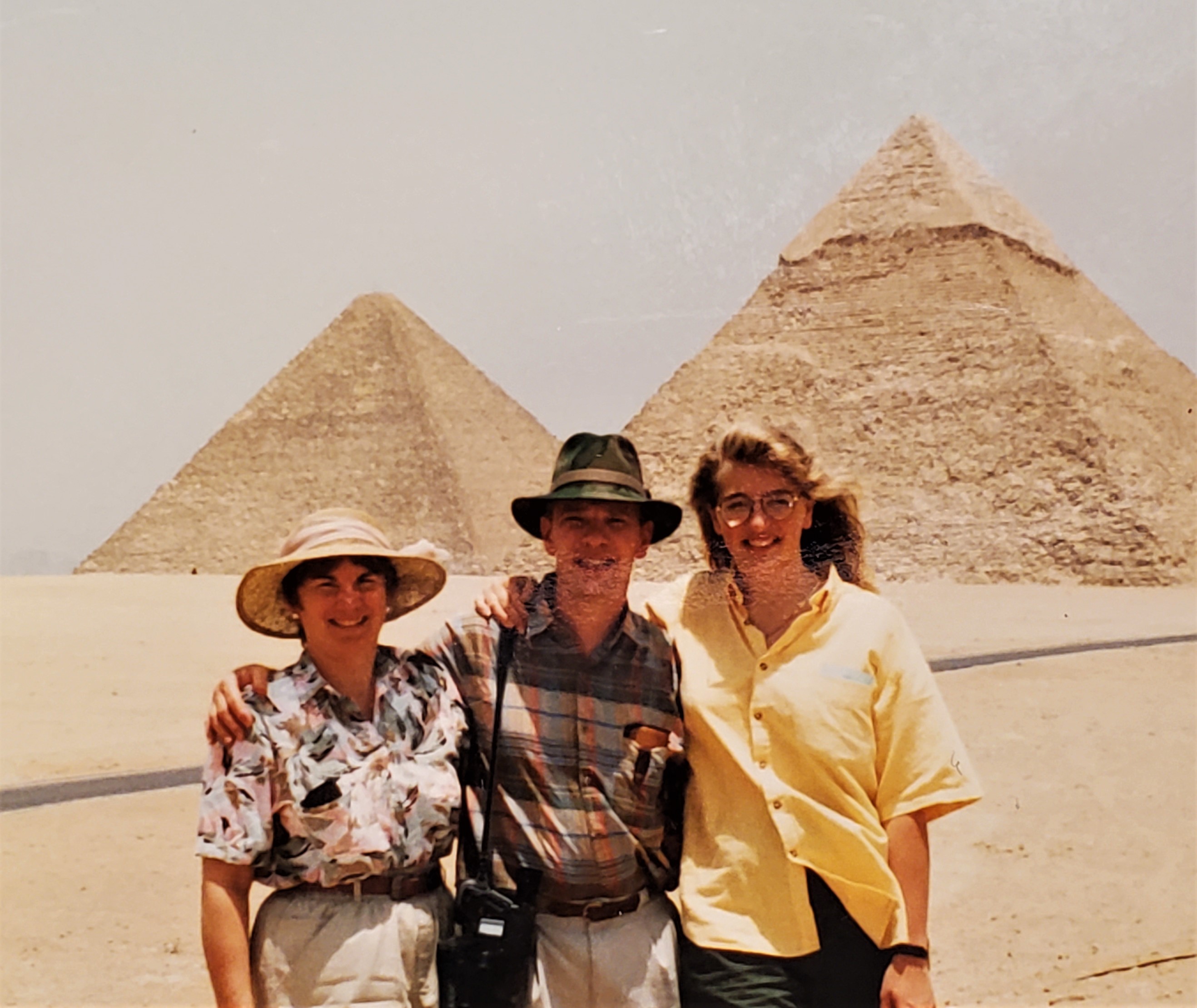 Three people standing arm in arm in front of the egyptian pryramids in 1990
